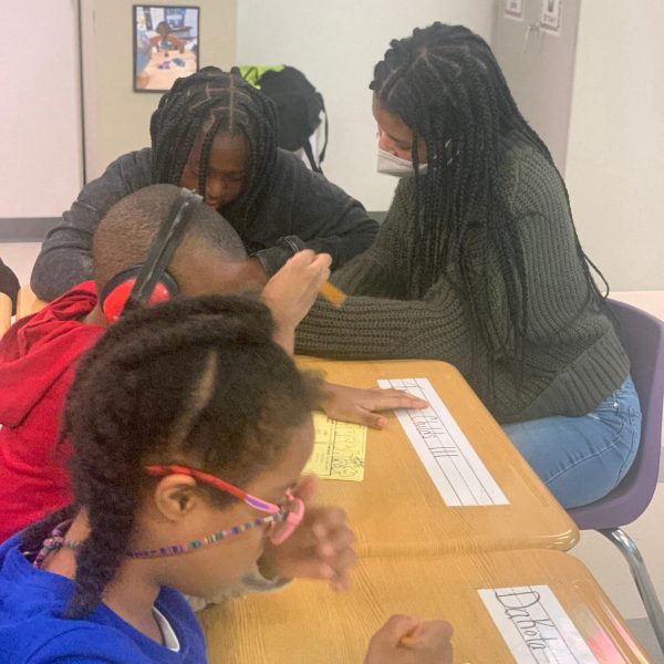 Founder Eden Wilson in a classroom sitting at a desk helping a student with handwriting